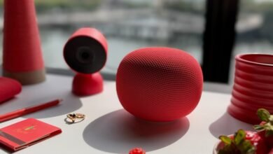 Red smart speaker and camera on a white desk with decorative items.