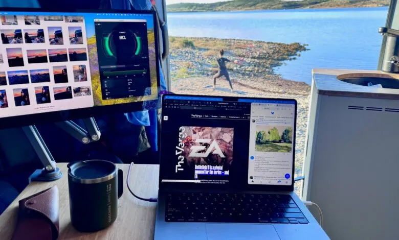 Laptop and monitor setup inside a van with a scenic lake view and a person doing yoga outdoors.