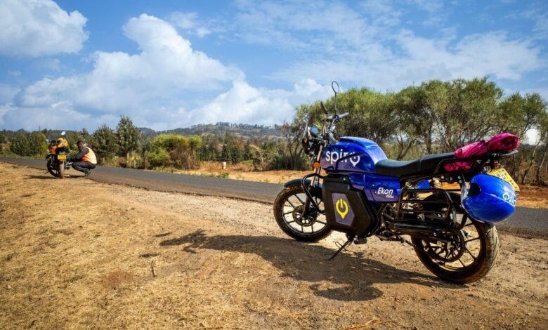 A bright blue electric motorcycle with 'Spirit' and 'Ekon' branding parked on a dirt road.