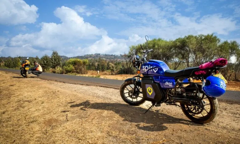 A bright blue electric motorcycle with 'Spirit' and 'Ekon' branding parked on a dirt road.