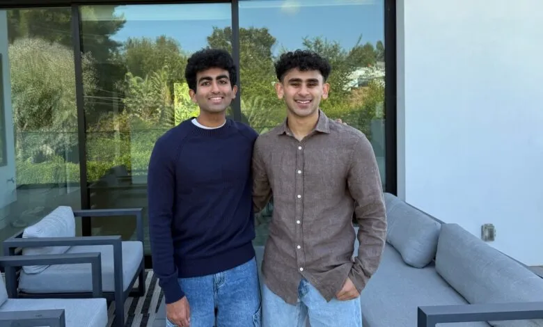 Two young men smiling and posing outdoors on a patio with modern furniture.