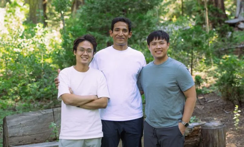 Three young men smiling and posing for a photo in a forest setting.
