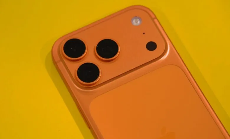 Close-up of the rear camera array of an orange iPhone on a yellow background.