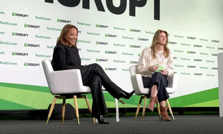 Two women sitting on chairs on a stage at a TechCrunch Disrupt event.