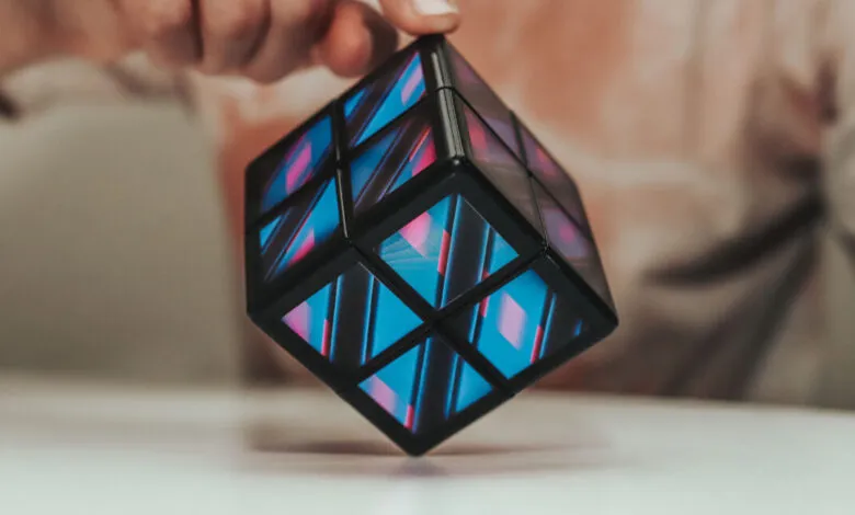 Close-up of a person's fingers holding a futuristic cube with glowing blue and pink patterns.
