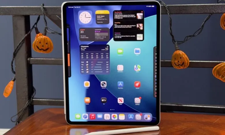 An iPad Pro displaying widgets and apps, with Halloween pumpkin lights in the background.