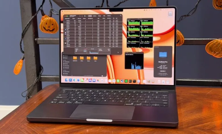 A dark MacBook Pro displays system monitoring tools with Halloween-themed string lights.