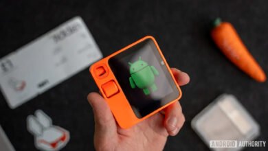 Hand holding an orange Rabbit R1 device displaying the Android mascot.