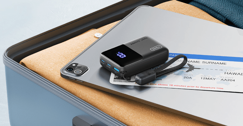 Compact black power bank with digital display on a tablet, next to a plane ticket.