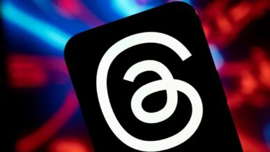 Close-up of a smartphone displaying the Threads app logo against a blurred background of red and blue lights.