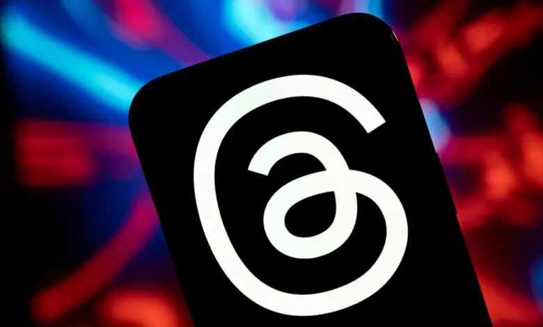 Close-up of a smartphone displaying the Threads app logo against a blurred background of red and blue lights.