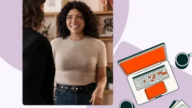 A smiling woman in a beige sweater talks to someone off-camera, with a laptop and coffee on a purple background.
