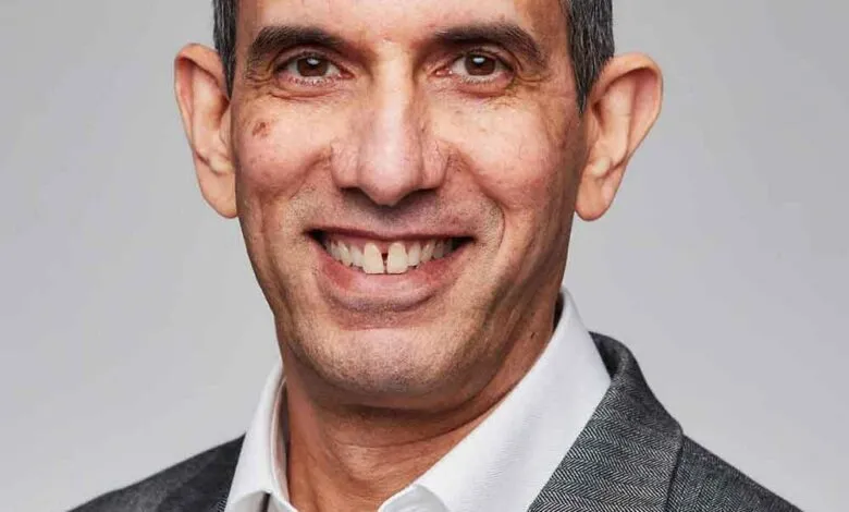 Portrait of Kamal Hathi smiling warmly, wearing a grey suit and white shirt.