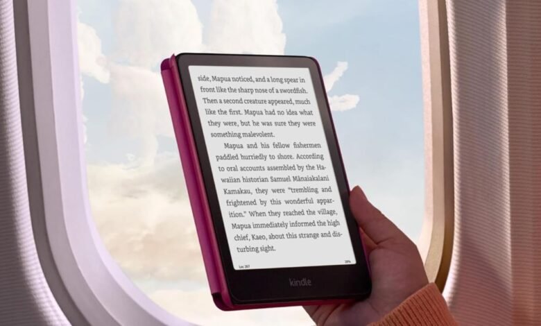 Hand holding a pink Kindle Paperwhite e-reader by an airplane window.