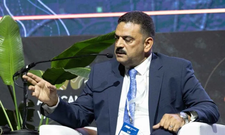 Man in a suit speaking at a conference, gesturing with his hand.