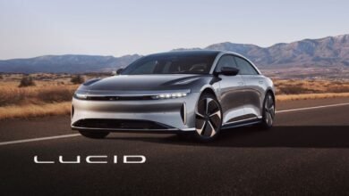 Silver Lucid Air electric sedan driving on a desert highway with mountains in the background.