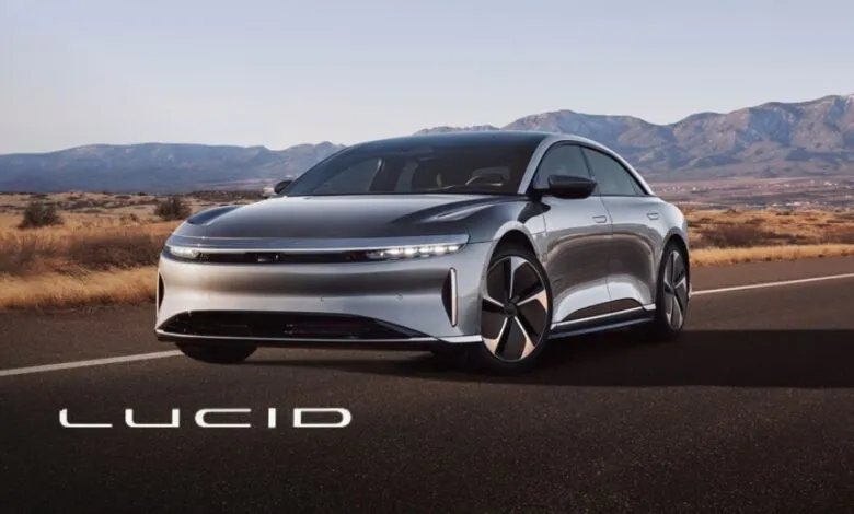 Silver Lucid Air electric sedan driving on a desert highway with mountains in the background.