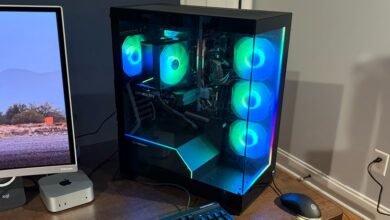 A gaming PC with RGB lighting, a monitor displaying a desert landscape, and computer peripherals.