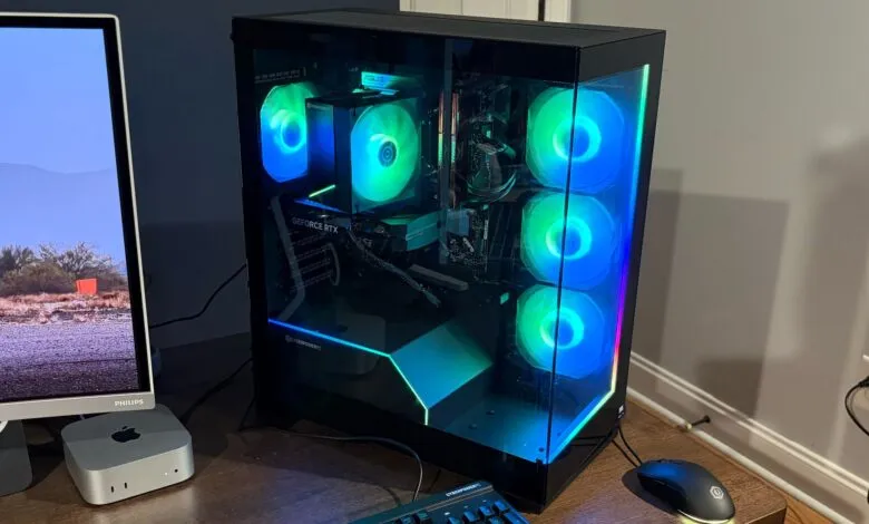 A gaming PC with RGB lighting, a monitor displaying a desert landscape, and computer peripherals.