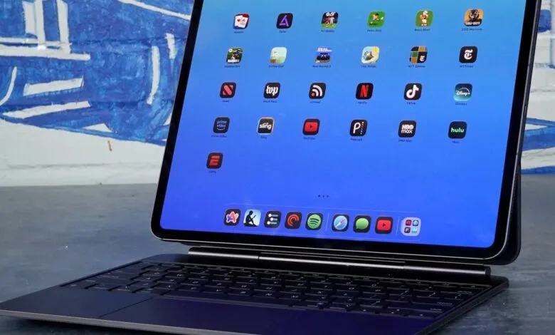 Close-up of an iPad Pro with a Magic Keyboard, displaying a grid of popular app icons on a vibrant blue screen.