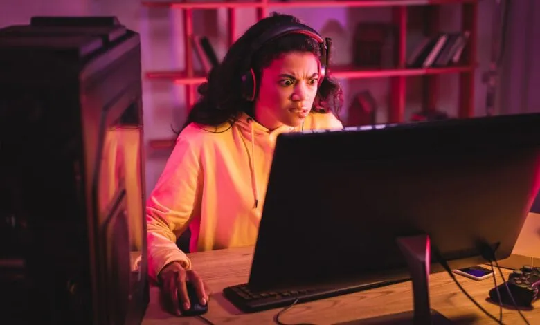 Young woman wearing headphones, intensely focused on a computer screen with a frustrated expression.
