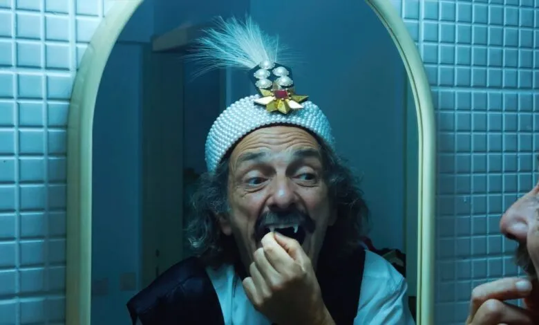 Man in a turban with fake fangs checking his teeth in a mirror.