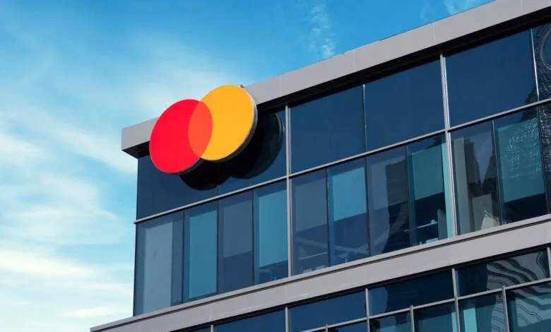 Mastercard logo on a modern glass building exterior against a blue sky.