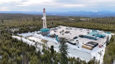 Aerial view of a winter oil drilling site surrounded by snow-covered pine forest.
