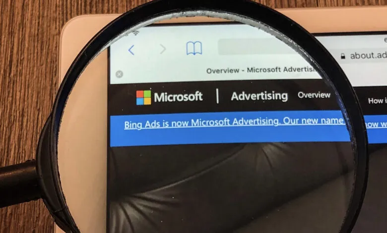 Magnifying glass over a tablet screen showing Microsoft Advertising website.