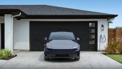Dark blue electric car parked in front of a modern garage with charging station.