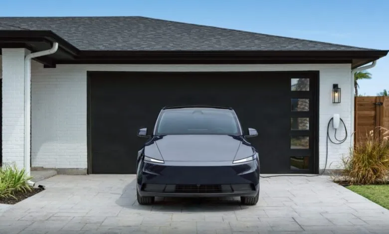 Dark blue electric car parked in front of a modern garage with charging station.