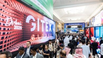 Crowd of people at GITEX Global technology exhibition in Dubai with large digital displays.