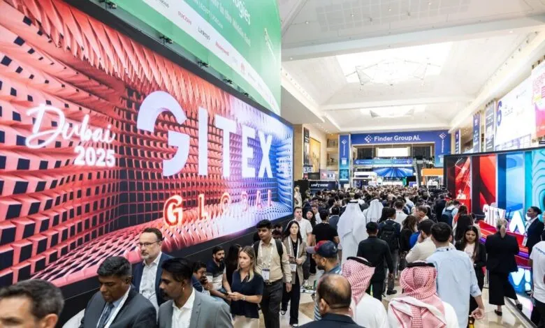 Crowd of people at GITEX Global technology exhibition in Dubai with large digital displays.