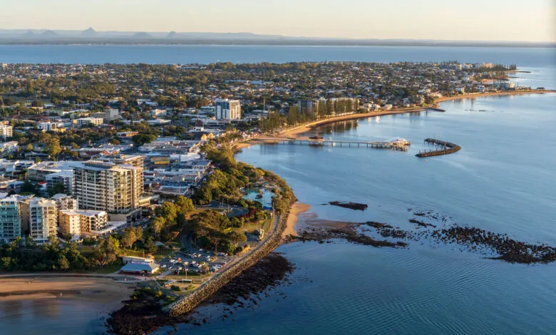 Aerial view of a coastal town with buildings, a pier, and the ocean at sunset.
