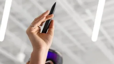 Close-up of a hand holding a black stylus pen, with VR goggles visible below.