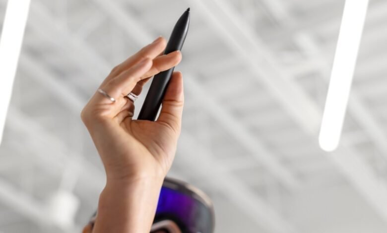 Close-up of a hand holding a black stylus pen, with VR goggles visible below.