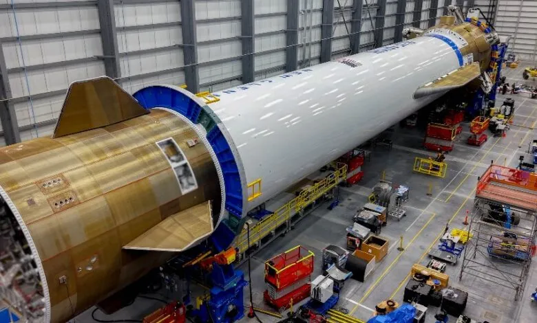 A large rocket section with fins and a white cylindrical body is assembled in a factory.