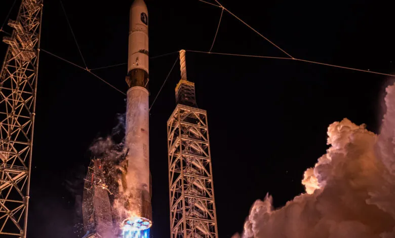 A rocket launches into the night sky, illuminated by its engines and surrounding launch tower.