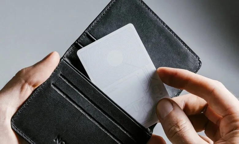 A hand places a white tracking card into a black leather wallet.