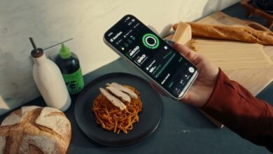 Person holding a smartphone displaying a nutrition tracking app next to a meal.
