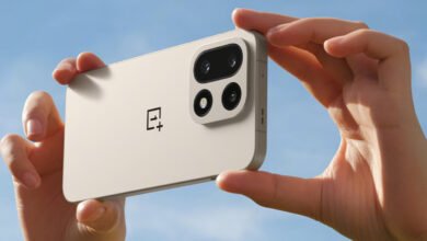 Hands holding a light beige OnePlus smartphone, showcasing its camera module against a blue sky.