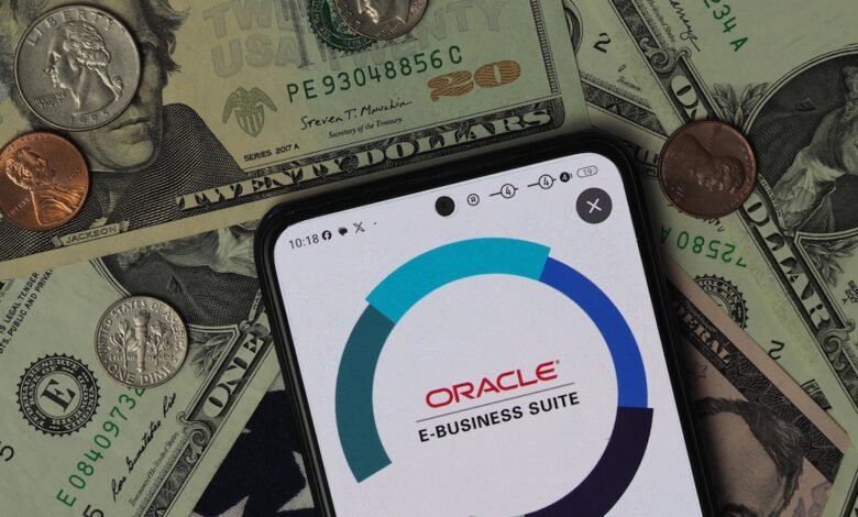 Smartphone displaying Oracle E-Business Suite logo over US dollar bills and coins.