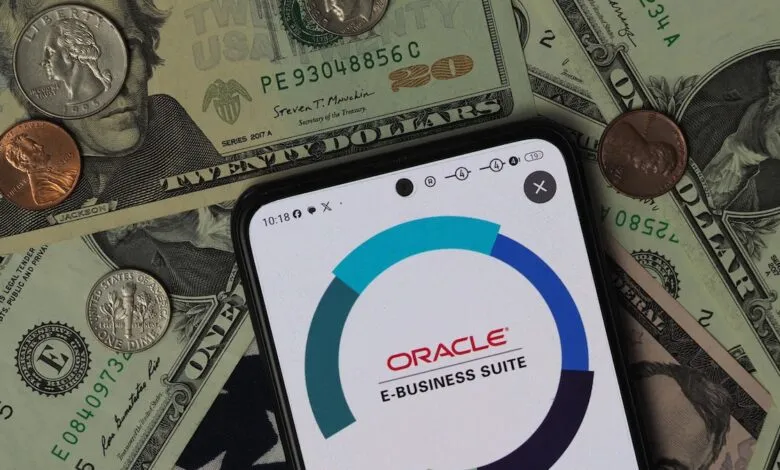 Smartphone displaying Oracle E-Business Suite logo over US dollar bills and coins.