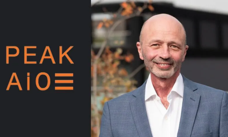 Man in a suit smiling next to the PEAK AiO logo