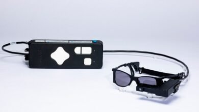 A black control unit and a pair of black augmented reality glasses on a white background.