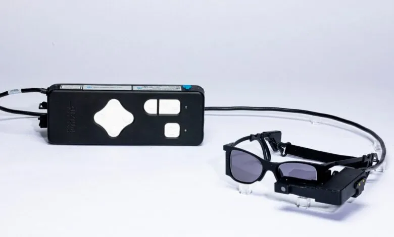 A black control unit and a pair of black augmented reality glasses on a white background.