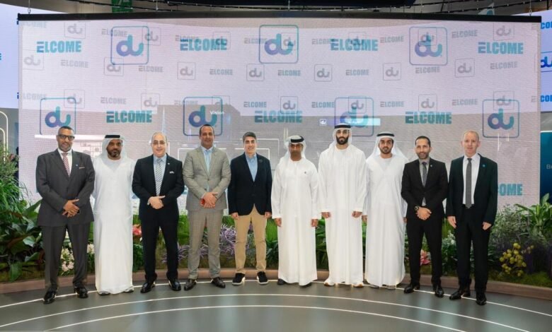Group of men in suits and traditional attire posing in front of a large screen displaying the 'du' logo and 'WELCOME' text.