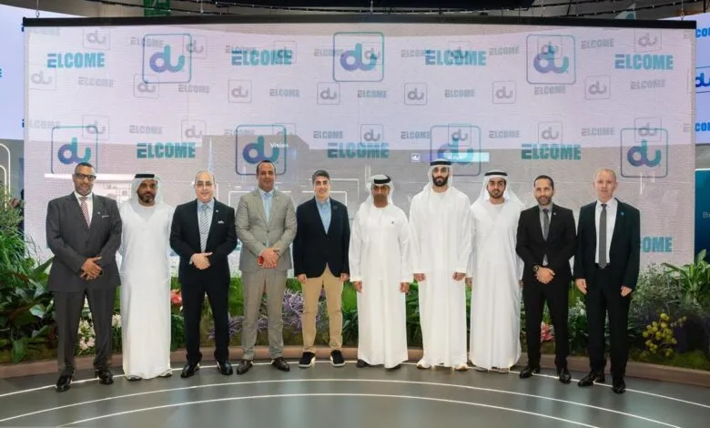 Group of men in suits and traditional attire posing in front of a large screen displaying the 'du' logo and 'WELCOME' text.