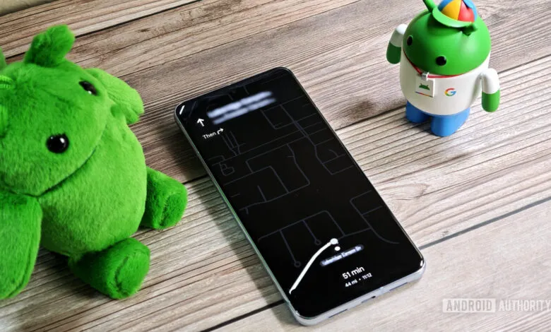 Smartphone displaying Google Maps navigation with a plush green character and Android figurine nearby.