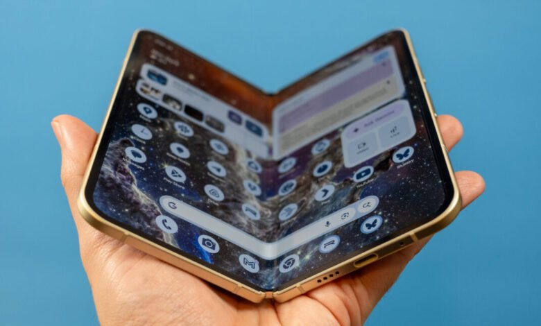 A hand holds a gold-colored foldable smartphone open, displaying a galaxy wallpaper and app icons.